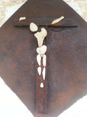 Rückseite eines alten Kanaldeckels mit einer Winkelverstärkung die als Kreuz dient. Figur aus gesammelten Steinen